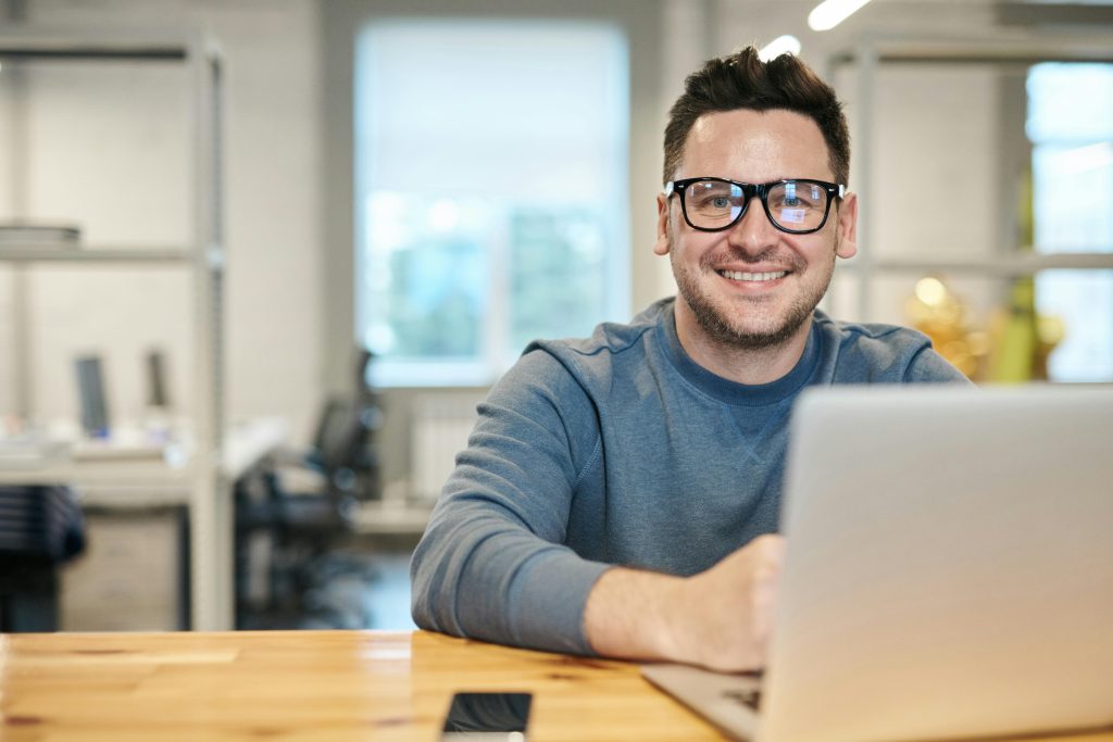 pexels-photo-3184611-3184611 Happy man wearing glasses working remotely on laptop in modern office environment.