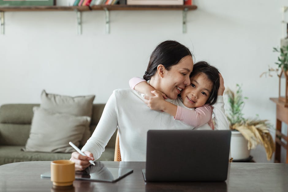 pexels-photo-4474036-4474036 Happy young Asian woman working remotely from home with laptop and tablet while adorable little daughter hugging from behind